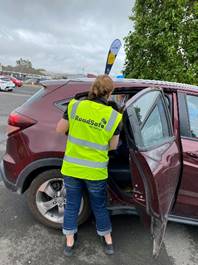 A person in a reflective vest standing in the back of a car

Description automatically generated